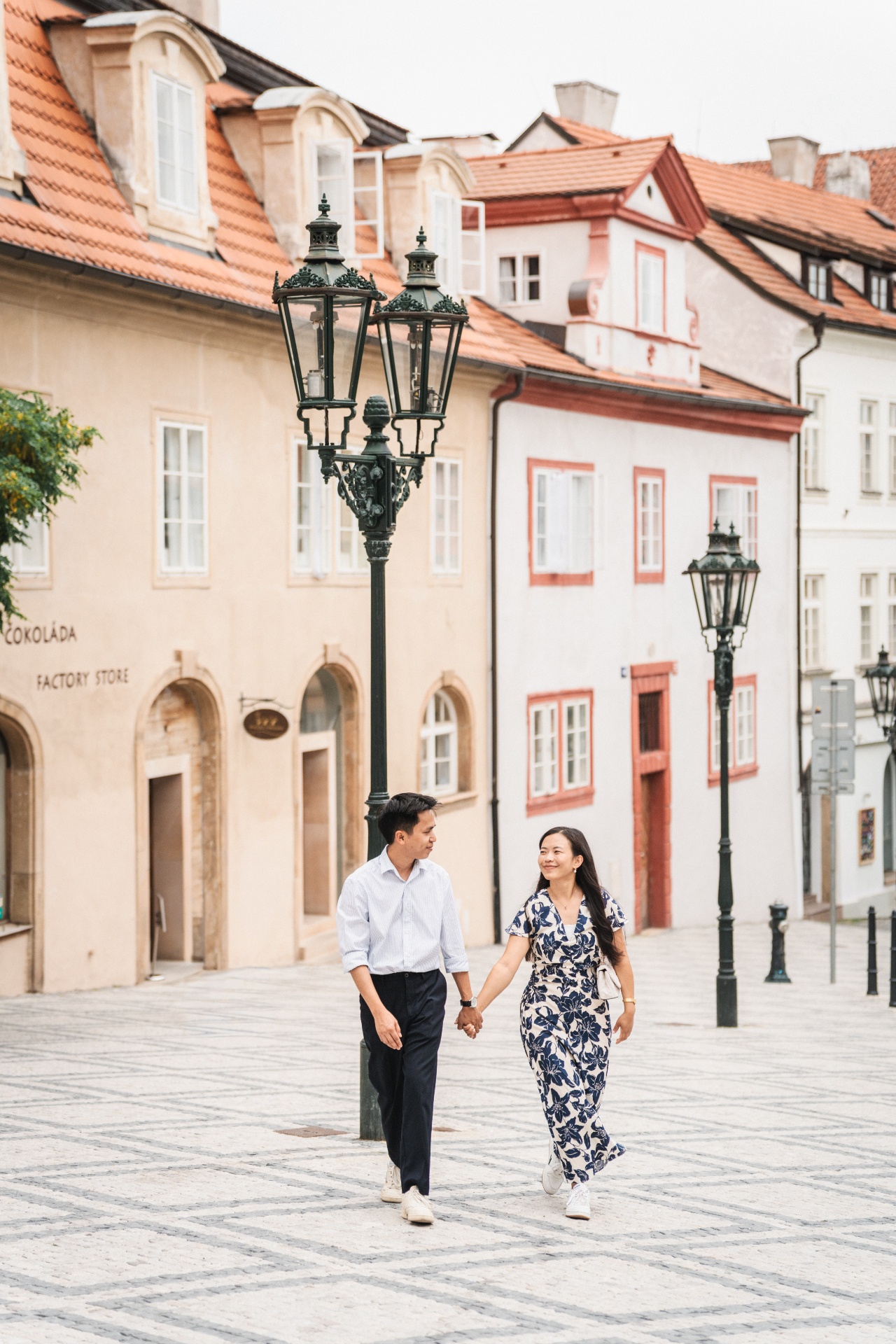 Couple holding hands walking through a quiet Prague street with vintage lampposts
