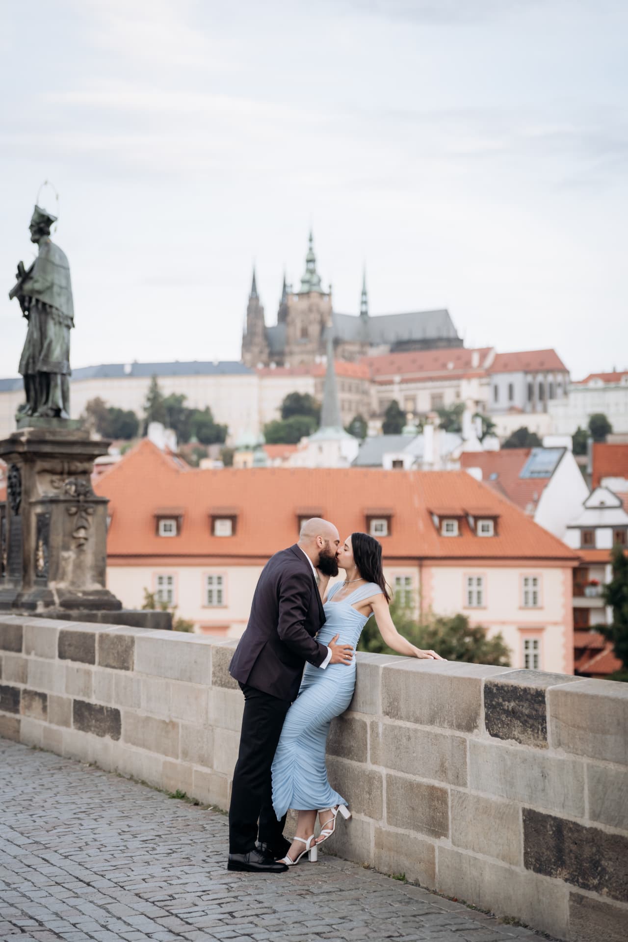 Couple kissing on Charles Bridge with Prague Castle and St. Vitus Cathedral in the background