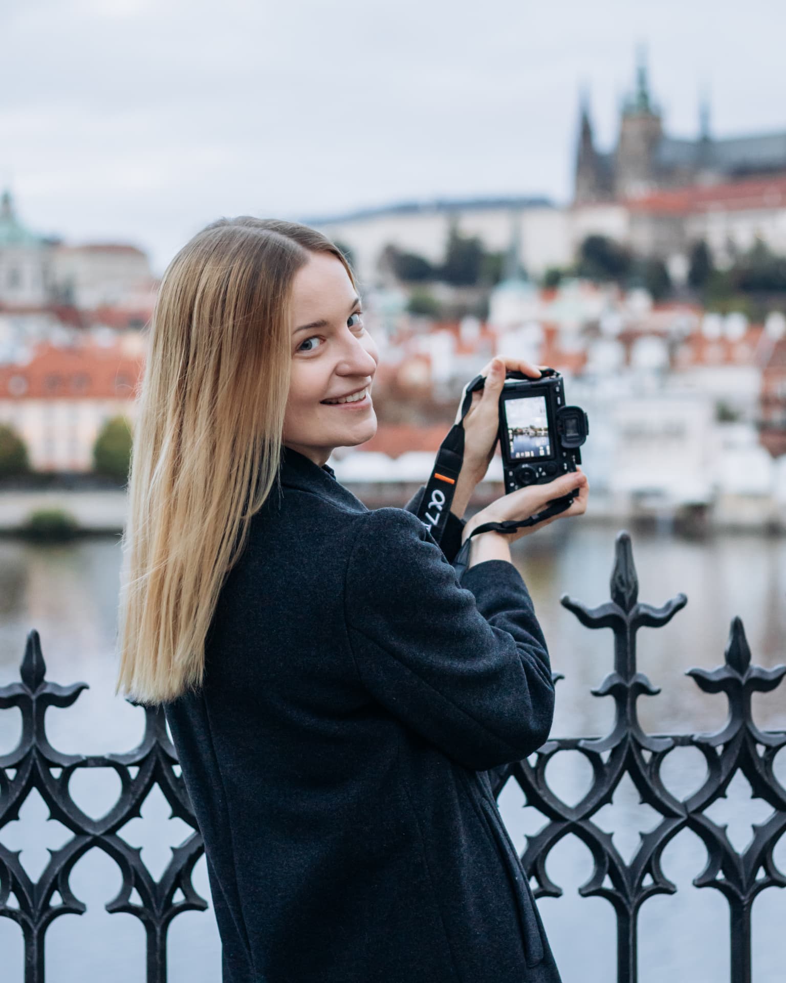 Marta Gawronska, lifestyle photographer in Prague, on a bridge over the Vltava with Prague Castle behind her