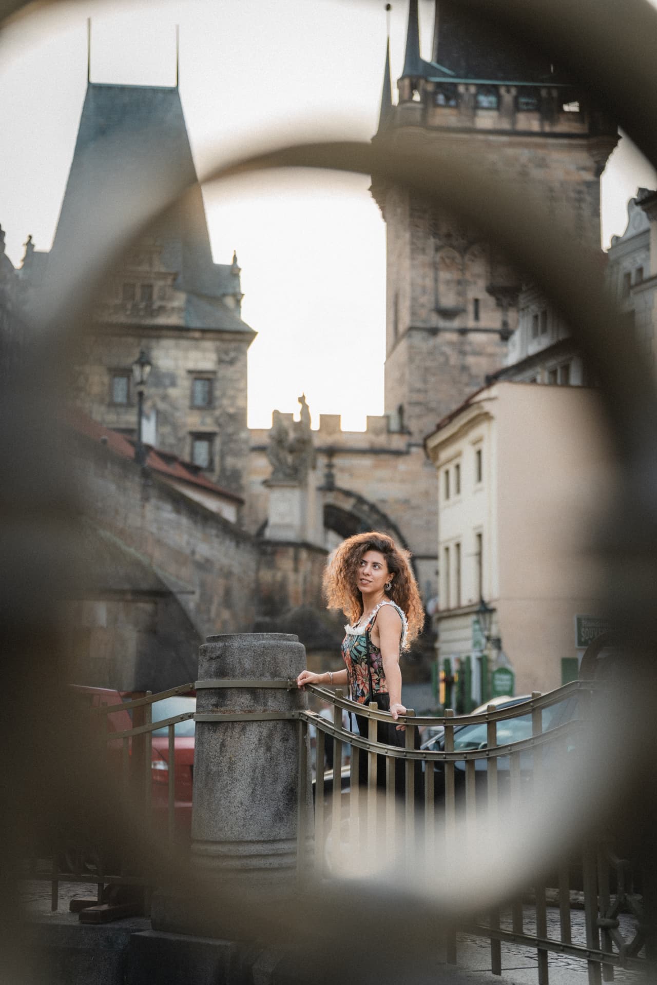 Prague photoshoot of a woman with curly hair framed by an arch with the Charles Bridge towers behind her